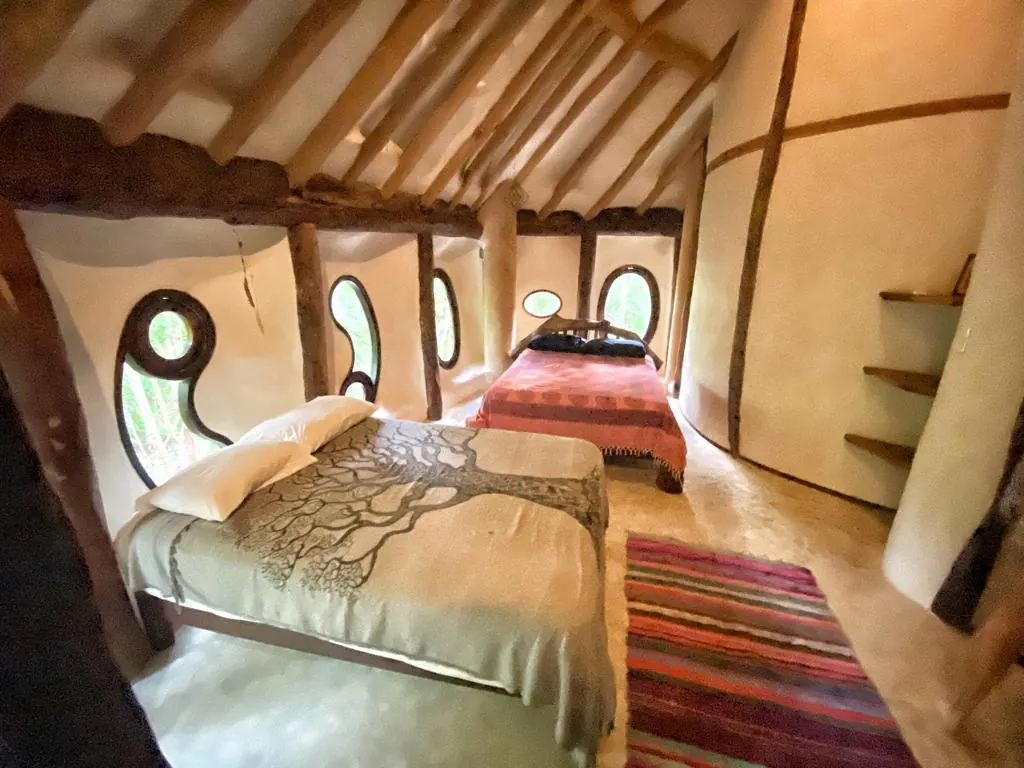 A jungle lodge room with two beds under a wooden roof